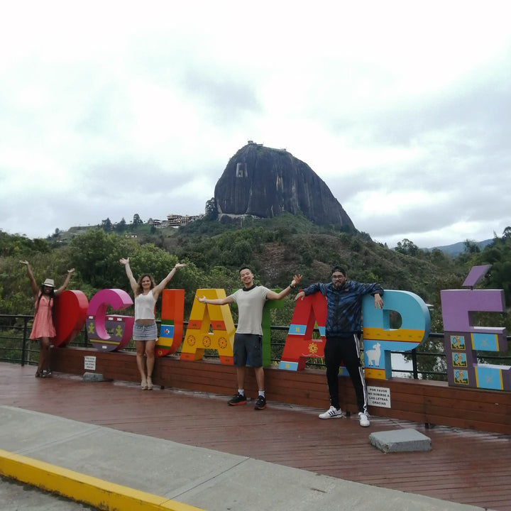 Grupo de personas frente a la piedra del peñol y letrero de Guatapé. 