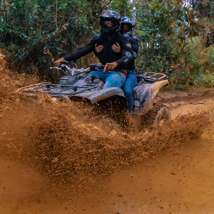 Personas manejando ATVs por caminos abiertos rodeado de lodo.