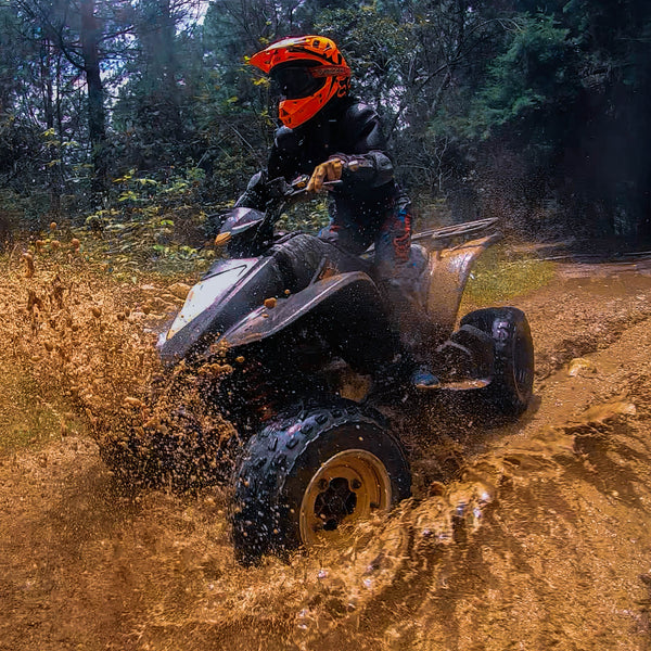 Persona manejando ATVs por caminos abiertos rodeado de lodo.