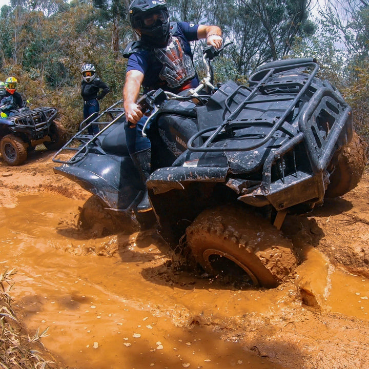 Persona manejando ATVs por caminos abiertos rodeado de lodo.