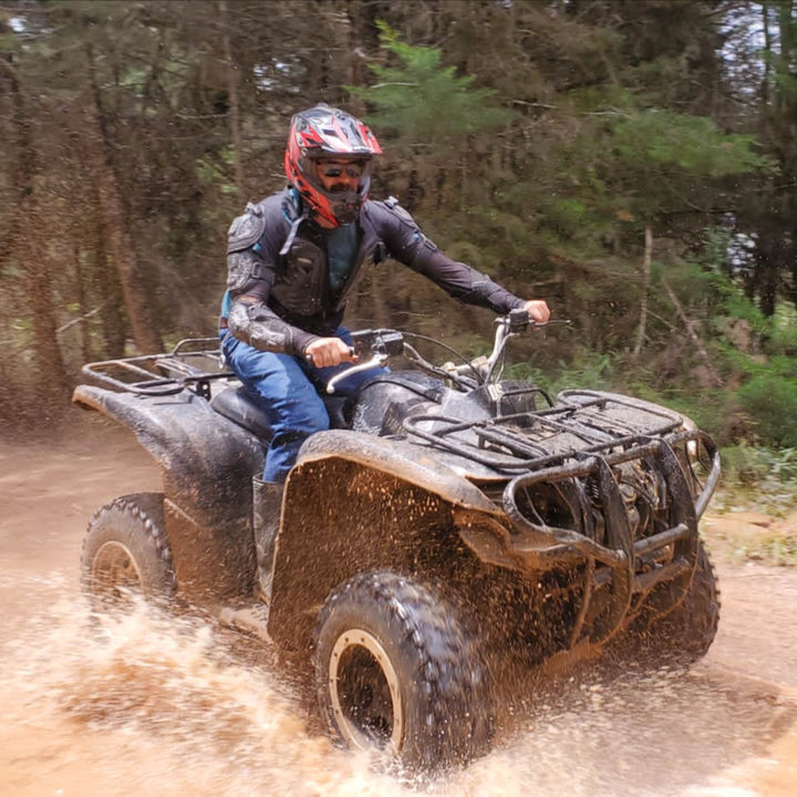 Persona manejando ATVs por caminos abiertos rodeado de lodo.